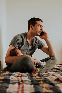 Father holding his baby while using his phone