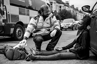 Male paramedic checking on an injured woman on a road