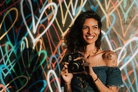 Cheerful woman using an instant camera against the backdrop featuring the graffiti artwork by James Goldcrown in Los Angeles, USA, 13 July 2018 
