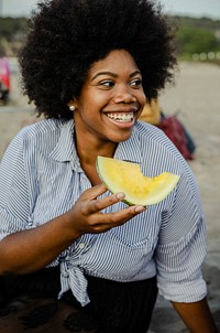 Woman eating a watermelon at a beach picnic