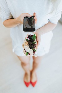 Woman taking a photo of a toast with blackberry jam and vegan cream cheese