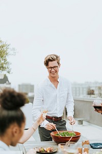 Man serving a salad to his friends at a rooftop party