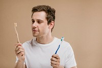 Man in a white tee choosing between a wooden toothbrush and a plastic one