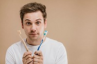 Man in a white tee choosing between a wooden toothbrush and a plastic one