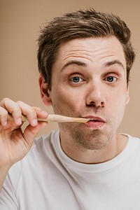 Blond man brushing his teeth with a wooden toothbrush