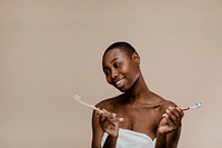 Black woman in a towel choosing between a wooden toothbrush and a plastic one