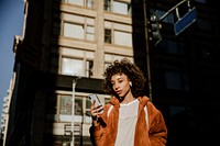 Cheerful black woman listening to music while walking in downtown