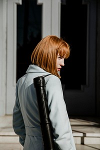 Female artist in a gray coat carrying a black poster tube on her shoulder