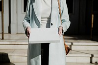 Woman in an overcoat carrying a white box in front of a building