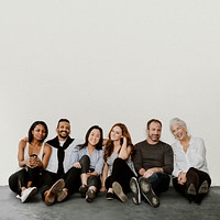 Group of cheerful diverse people sitting on a floor in a white room