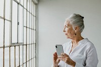 Senior woman using a phone by the window in a white room in a white room