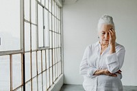 Stress senior woman standing by the window in a white room