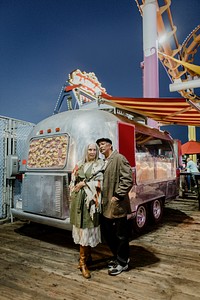 Cool senior couple standing by the food truck inside of an amusement park