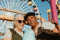 Cheerful elderly couple taking a selfie with cotton candy at Pacific Park in Santa Monica, California