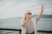 Senior woman on the phone waving by the sea