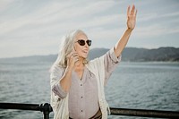 Senior woman on the phone waving by the sea