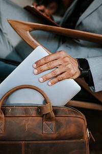 Man in a gray suit grabbing his laptop from a brown leather bag