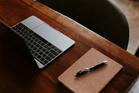 Laptop by a notepad on a wooden table in the office