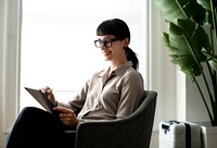 Woman using a stylus with her digital tablet while waiting for her flight in an airport lounge