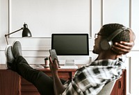 Black man with headphones playing on his phone sitting at his desk