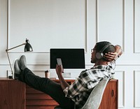 Black  man with headphones playing on his phone sitting at his desk