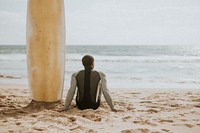 Black man sitting by his surfboard