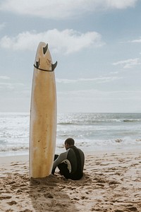 Black man sitting by his surfboard