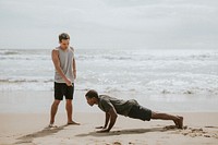 Black man doing pushups with a trainer at the beach