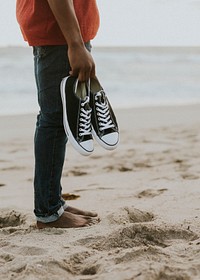 Black man carrying his shoes on the beach