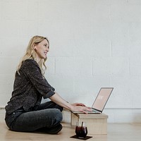 Cheerful blond woman using a laptop on a wooden floor