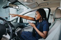 Happy black woman with her phone pointing in the car
