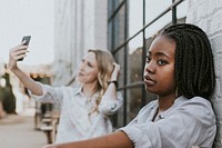 Black woman getting bored of her blond friend keep taking a selfie