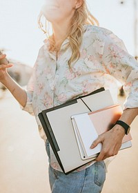 White woman with file folders crossing a street while using her phone