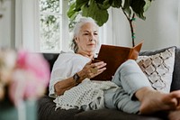 Elderly woman reading a book on a sofa in a weekend