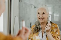Elderly woman putting on a makeup in front of a mirror