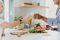 Cheerful elderly clinking their white wine in a kitchen