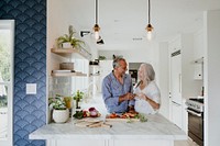 Cheerful elderly clinking their white wine in a kitchen