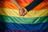 Gay couple holding hands in front of a rainbow flag signifying support and love