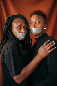 Lesbian couple wearing tapes on their mouth against a red background