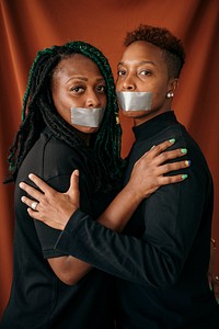 Lesbian couple wearing tapes on their mouth against a red background