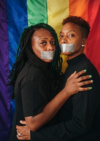 Lesbian couple wearing tapes on their mouth against a rainbow background