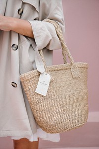 Woman in a beige coat carrying a straw bag with a branding tag mockup
