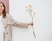 Woman holding a branch of yellow forsythia over a white wall