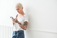 Tattooed woman using her phone by the white wall