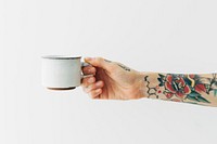 Tattooed hand holding a white coffee cup