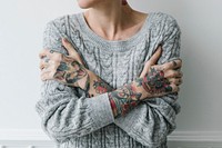 Tattooed woman in a gray sweater hugging herself