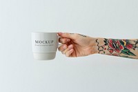 Tattooed hand holding a white coffee cup mockup