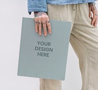 Tattooed woman in a blue linen shirt holding a book mockup