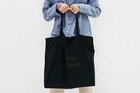 Tattooed woman in a blue linen shirt holding a black tote bag mockup