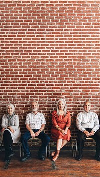 Diverse elderly people sitting in a row against a brick wall background